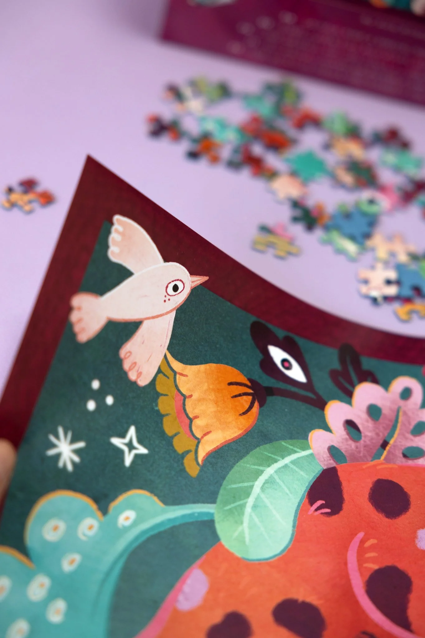 A colorful image of a bird and leaves on a dark green background, with a pile of puzzle pieces scattered on a purple surface in the background.