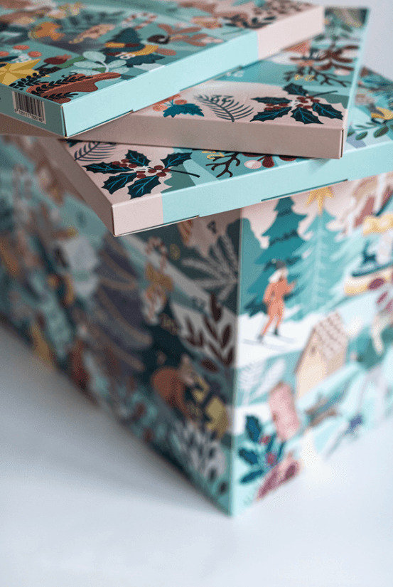 Close-up of three decorated boxes with winter and holiday themes, featuring holly, Christmas trees, and snow scenes.