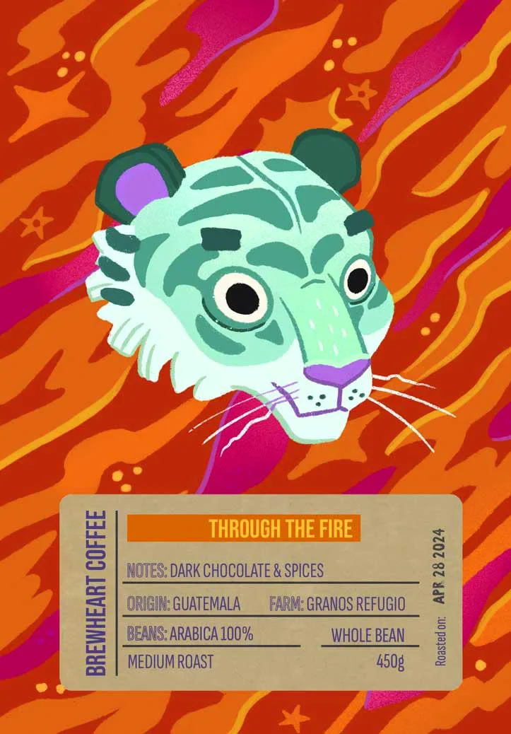 Illustration of a tiger's head with a green and white face, purple nose and ear tips, set against a fiery orange, red, and purple background, with a coffee label titled 'Through the Fire'.