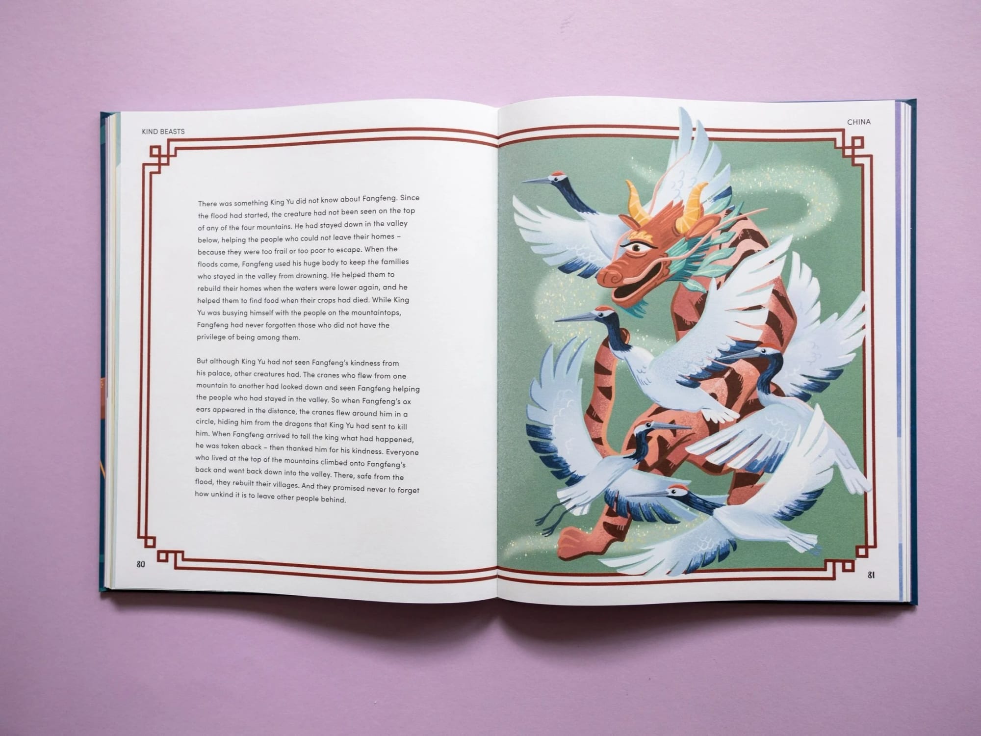 An open book showing a colorful illustration of a dragon and several cranes flying around it, with a pink background.