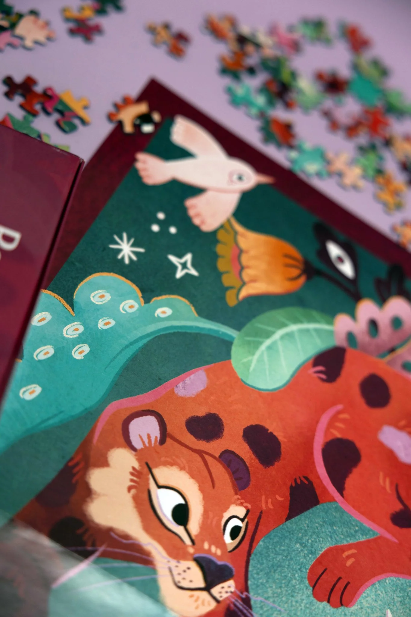 Close-up of a colorful illustrated children's book page featuring a jaguar lying on green leaves with a background of whimsical plants and patterns, along with scattered puzzle pieces in the background.